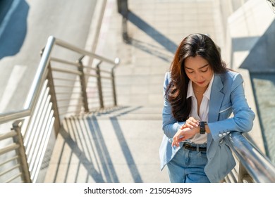 Asian businesswoman office worker looking time on hand watch while walking up stairs in railway station urban city. Business woman go to working at office building district in morning rush hour - Shutterstock ID 2150540395