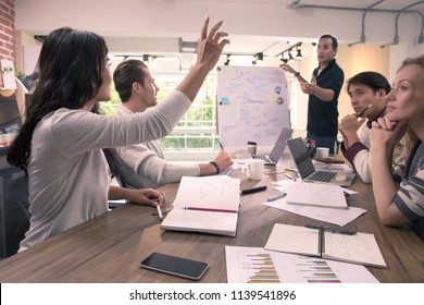 Asian Businesswoman Raising Hand And Asking Questions And Discussing To Businessman During Team Business Meeting In Modern Office, Diverse Group Of Colleagues People Looking To Her With Interesting.