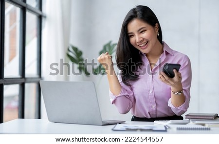 Asian businesswoman raising her hand with a happy expression and looking at her phone The businesswoman was delighted to receive an email informing her of her annual bonus. concept of success