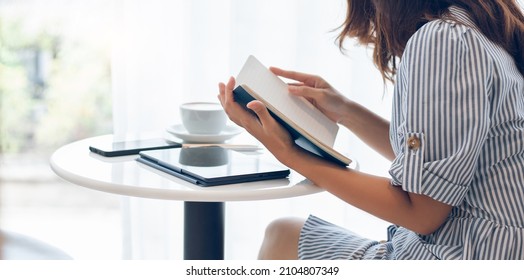 Asian Businesswoman Reading An Appointment In Note Book During A Break With Coffee Drink, On White Table Have Digital Tablet And Mobile Phone Use For Working Online