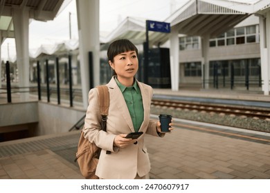 Asian businesswoman with smart phone and coffee waiting for the train at the train station - Powered by Shutterstock