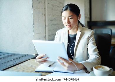 Asian Businesswoman With Tablet Watching Online Video In Modern Cafe