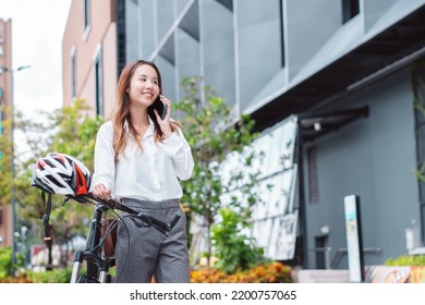 Asian Businesswoman Use Smart Mobile Phone During Go To Office Work At City Street With Bicycle, Happy Female Commuting Outside In Morning, Eco Friendly People Lifestyle Concept.