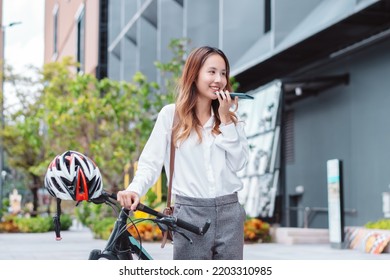 Asian Businesswoman Use Smart Mobile Phone During Go To Office Work At City Street With Bicycle, Happy Female Commuting Outside In Morning, Eco Friendly People Lifestyle Concept.