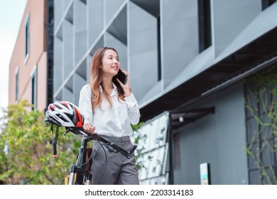 Asian Businesswoman Use Smart Mobile Phone During Go To Office Work At City Street With Bicycle, Happy Female Commuting Outside In Morning, Eco Friendly People Lifestyle Concept.