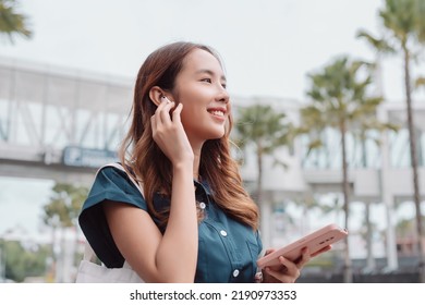 Asian Businesswoman Use Wireless Earbuds Listening Music In The Modern City Near Office
