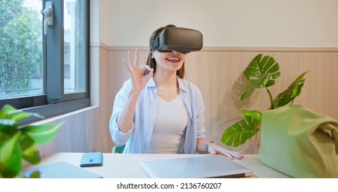 asian businesswoman uses metaverse augmented reality technology for work with ok gesture at workplace
