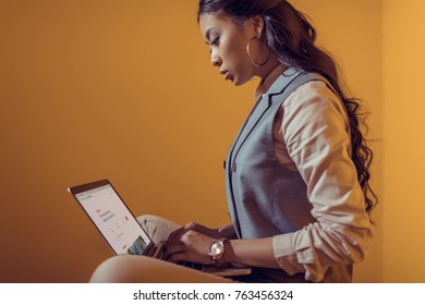 Asian Businesswoman Using Laptop With Airbnb Website In Front Of Orange Wall