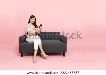 Asian businesswoman using mobile phone and sitting on sofa isolated on pink background