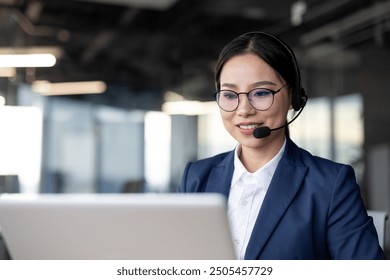 Asian businesswoman wearing headset works on laptop in modern office, showcasing professional customer service skills and confidence. - Powered by Shutterstock