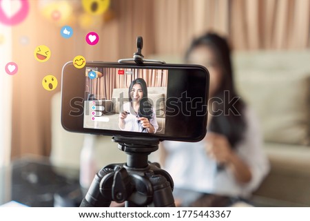 Asian businesswoman working from home live video interaction with customers using camera device vlogging selling make up products, viral internet social media influencer interacting to live audience