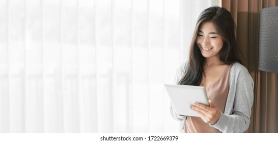 Asian businesswoman working at home using tablet device, browsing internet playing social media in video call meeting with colleagues and coworkers planning innovative ideas, quarantine self-isolation