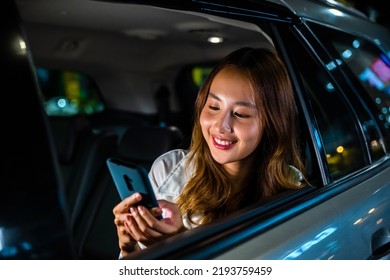 Asian businesswoman working late commuting from office in Taxi backseat with mobile phone in city at night after late work, Happy beautiful woman texting smartphone sitting car back seat in urban