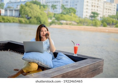 Asian businesswoman working online at the beach. Freelancer using technology for work everywhere. Woman talking with customer with mobile phone.