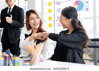 Asian businesswomen fist bump for the teamwork of business mergers and acquisitions for successful negotiation. Two businesswomen fist bump with partners to celebrate a partnership and business deals. - Powered by Shutterstock