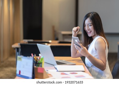 Asian businesswomen hapiness celebrating when checking success goal via technology laptop and mobile phone in modern office or coworking space, technology money wallet and online payment concept