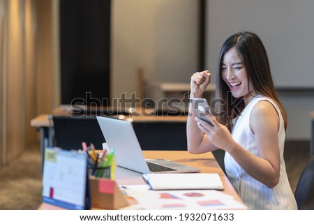 Asian businesswomen hapiness celebrating when checking success goal via technology laptop and mobile phone in modern office or coworking space, technology money wallet and online payment concept