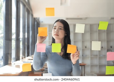 Asian businesswomen use post-it notes on glass walls to write strategy business plans to development grow to success,  in the office. - Powered by Shutterstock