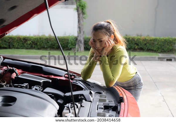 An asian bussiness woman has a car problem, she\
put hand under chin at broken car, looking to engine with boring,\
disappointed emotion.