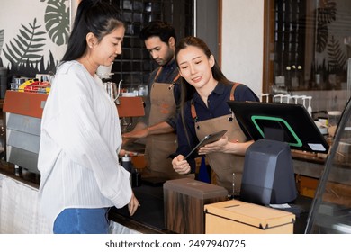 Asian cafe cashier worker female showing menu or cashless billing payment to customer, barista small business owner using technology tablet receives coffee order at workplace in restaurant coffee shop - Powered by Shutterstock