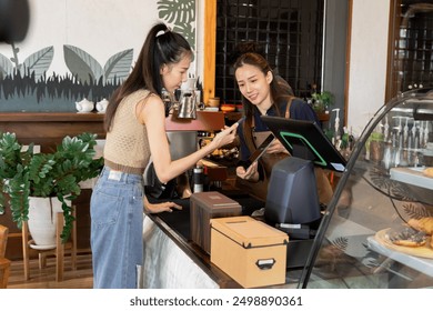 Asian cafe cashier worker female shows qr code digital billing to customer for scanning payment, barista small business owner using technology tablet receives coffee order at workplace in coffee shop - Powered by Shutterstock