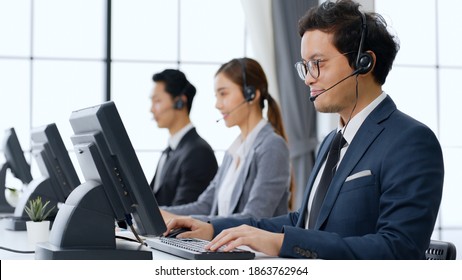 Asian Call Center Team, Customer Service, Telesales In Formal Suit Wearing Headset Or Headphone Talking With Customer In Modern Office