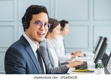 Asian Call Center Team, Customer Service, Telesales In Formal Suit Wearing Headset Or Headphone Talking With Customer In Modern Office