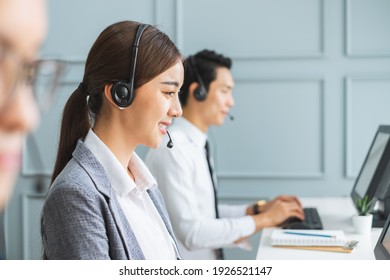 Asian Call Center Team, Customer Service, Telesales In Formal Suit Wearing Headset Or Headphone Talking With Customer In Modern Office