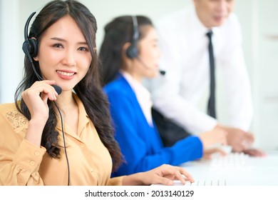 Asian Call Center Woman Smiling And Hold Headset With Team Working In Office Background