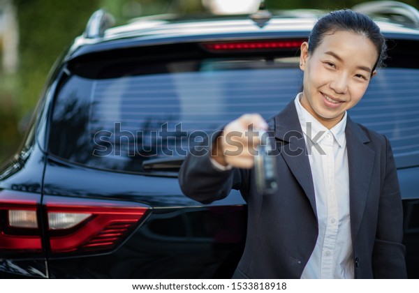 Asian car driver
woman smiling showing new car keys and car. Mixed-race Asian and
Caucasian girl.selective
focus