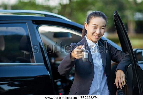 Asian car driver\
woman smiling showing new car keys and car. Mixed-race Asian and\
Caucasian girl.selective\
focus