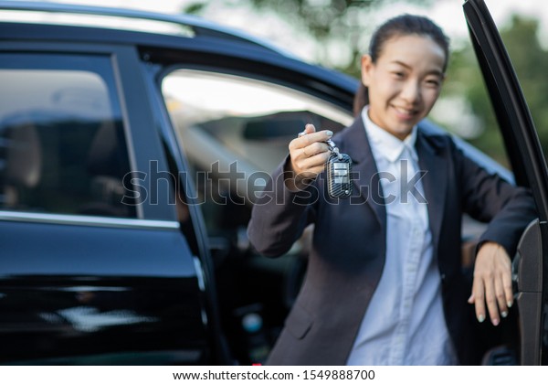 Asian car driver\
woman smiling showing new car keys and car. Mixed-race Asian and\
Caucasian girl.selective\
focus