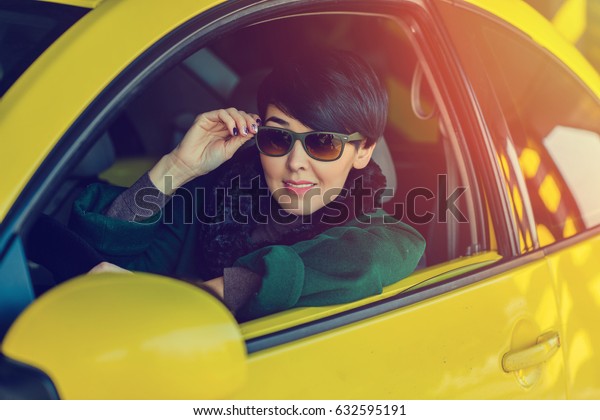 Asian car driver woman smiling in glasses with\
short hair,sits in yellow car.Mixed race Asian Caucasian\
girl.Portrait of a girl at\
sunset