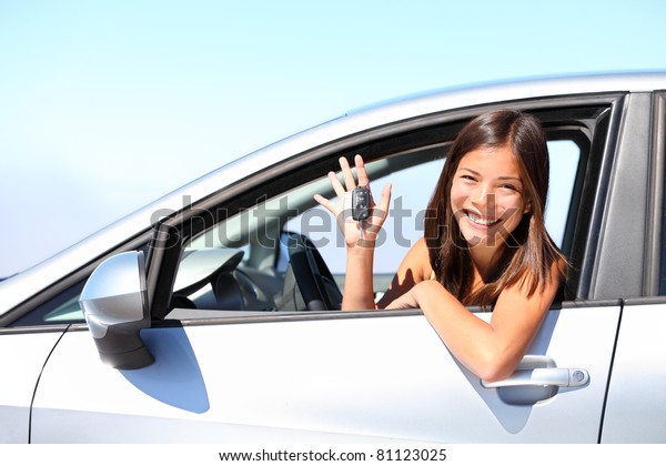 Asian car driver woman smiling\
showing new car keys and car. Mixed-race Asian and Caucasian\
girl.