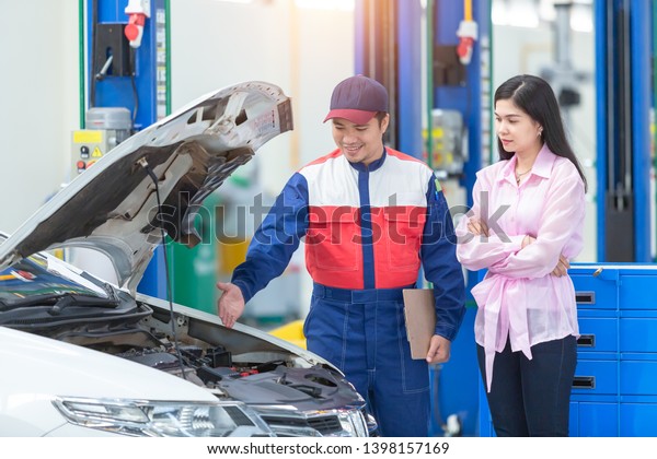 Asian\
car mechanic and customer Woman talking to a car mechanic in Car\
service center, both are standing next to the\
car.