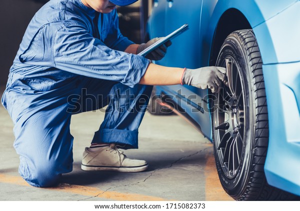 Asian car mechanic technician holding clipboard and\
checking to maintenance vehicle by customer claim order in auto\
repair shop garage. Wheel tire repair service. People occupation\
and business job