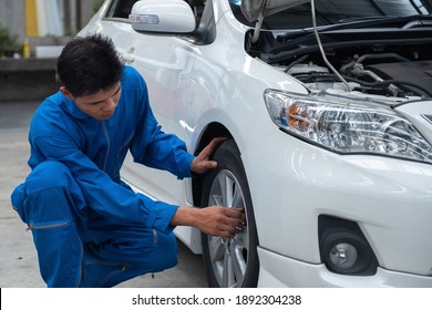 Asian Car Mechanic Technician Sitting And Checking Car Tyres Or Car Wheel In In Auto Repair Shop Garage. Wheel Tire Repair Service.