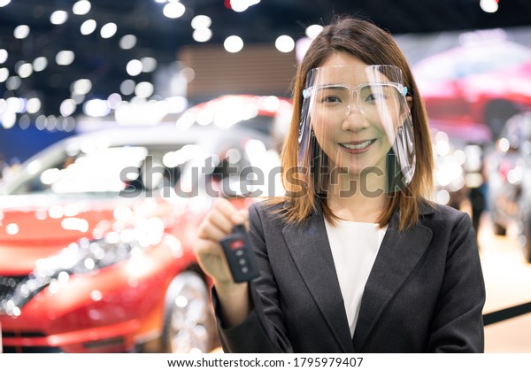 Asian car seller wearing face mask presents car\
and passing new car key to customer after purchased while\
coronavirus pandemic