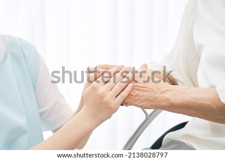 Asian caregiver holding Asian senior woman's hands, no face