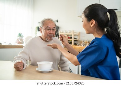 Asian Caregiver Nurse Serve Food To Senior Man Sitting On Dinner Table. Attractive Young Specialist Carer Woman Doctor Support And Taking Care Of Happy Older Elderly Mature Grandfather At Nursing Home