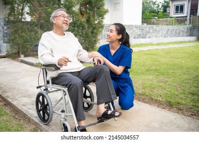 Asian Caregiver Nurse Take Care Senior Male Sit On Wheelchair Outdoor. Beautiful Specialist Girl Doctor Help And Support Elderly Mature Older Patient Man Doing Physical Therapy In Park At Nursing Home