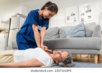 Asian caregiver saving senior woman's life by doing cpr in emergency. Attractive young female carer doctor doing first aid heart massage to unconscious patient with heart attack in living room at home - Powered by Shutterstock