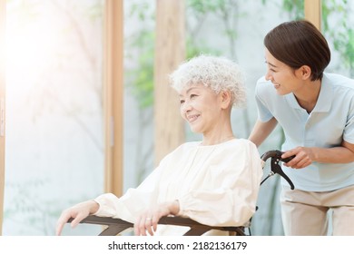 Asian Caregiver Talking To Woman In Wheelchair At Nursing Home