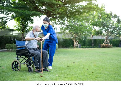 Asian Caregiver Wear Mask, Take Care Senior Disabled Man On Wheelchair. Young Beautiful Woman Carer Nurse At Nursing Home Support Disabled Elderly Man Patient To Walk With Walker Or Cane At Backyard.