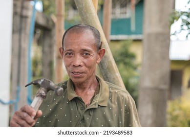 An asian carpenter holding a hammer. Wearing an old faded collared shirt. Rural livelihood concept.