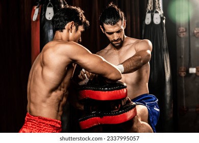 Asian and Caucasian Muay Thai boxer unleash knee attack in fierce boxing training session, delivering knee strike to sparring trainer, showcasing Muay Thai boxing technique and skill. Impetus