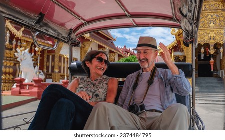Asian and Caucasian senior tourists having fun with touring around Chiang Mai by tuktuk taxi. They are excited with bargaining and taking taxi around town with stops at Buddhist temple. 