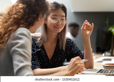 Asian and caucasian women teammates working together seated at desk in modern shared room, multiracial female colleagues discuss fresh ideas, doing common task using laptop thinking on project concept