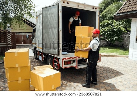 Asian and Caucasian workers in uniform unloading cardboard boxes from the truck. Delivery men unloading boxes and check the checklist with their coworkers. Professional delivery and moving service.