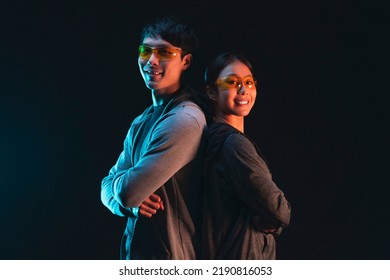 Asian Cheerful Confident Couple Male And Female Wearing Smart Glasses Standing Together Back To Back Casual Look At Camera Wearing Sport Active Cloth Studio Shot On Dark Background